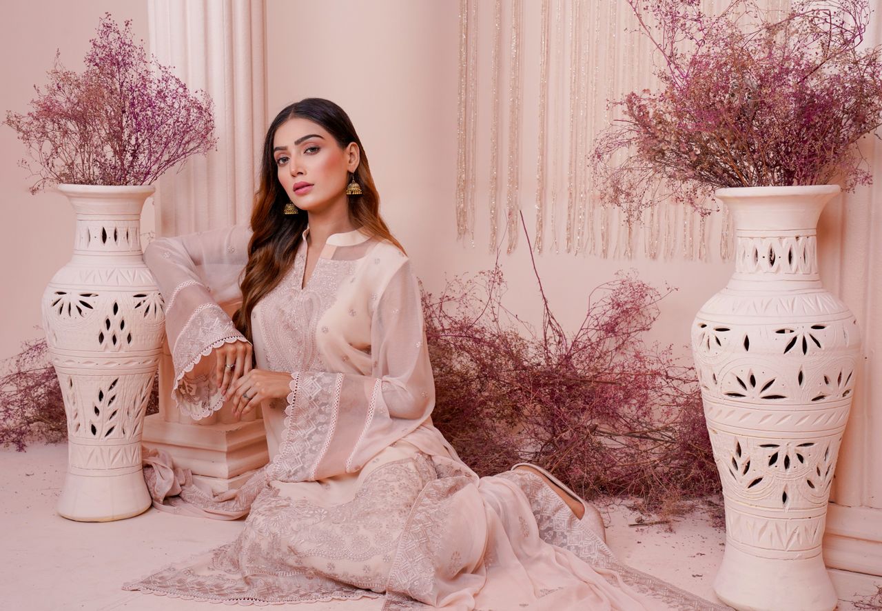 Elegant woman in a beautifully embroidered dress surrounded by decorative vases and dried flowers.