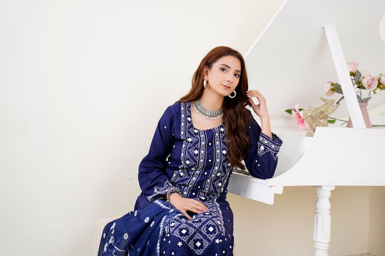 A fashionable woman in a blue traditional dress poses elegantly indoors by a white piano.