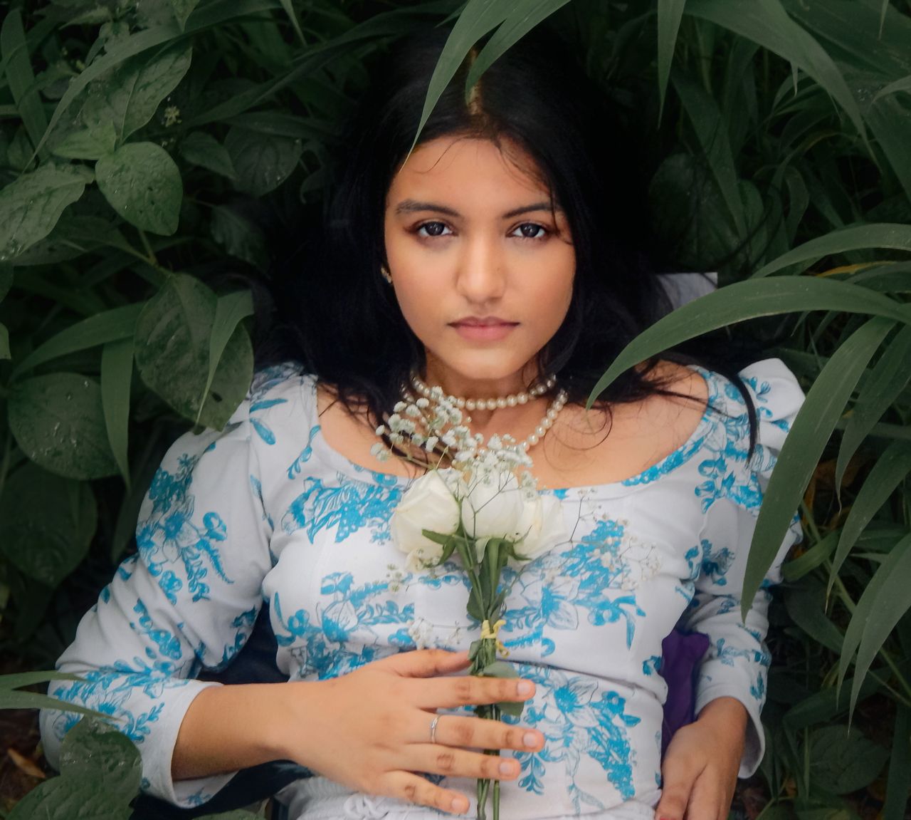 Elegantly styled portrait of a woman in a natural setting with a white floral dress and pearls.